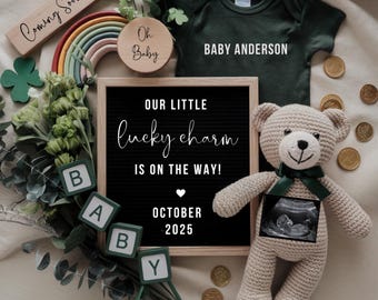 Op de afbeelding: Een zwart letterbord met de tekst "Our little lucky charm is on the way! October 2025". Naast het letterbord ligt een groene romper met de tekst "Baby Anderson". Op de voorgrond staat een gehaakte teddybeer met een echobeeld. Rondom de voorwerpen liggen groene klavertjes, een regenboog en gouden munten.