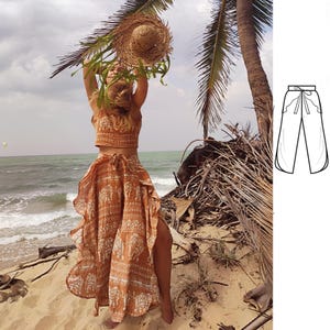 Pode incluir: Uma mulher vestindo um top cropped marrom e branco estampado e uma saia combinando com bainha franjada. A saia tem uma fenda lateral e é amarrada na cintura. A mulher está em pé em uma praia com uma palmeira ao fundo.
