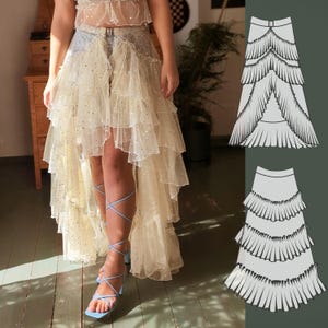 May include: A layered, high-low skirt in a light beige color, adorned with sparkling embellishments. The skirt features multiple tiers of flowing fabric, creating a dramatic effect. The design includes a belt and is paired with blue sandals.