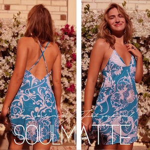 May include: A blue and white patterned mini dress with a criss-cross back strap. The dress has a V-neckline and a flowy silhouette.