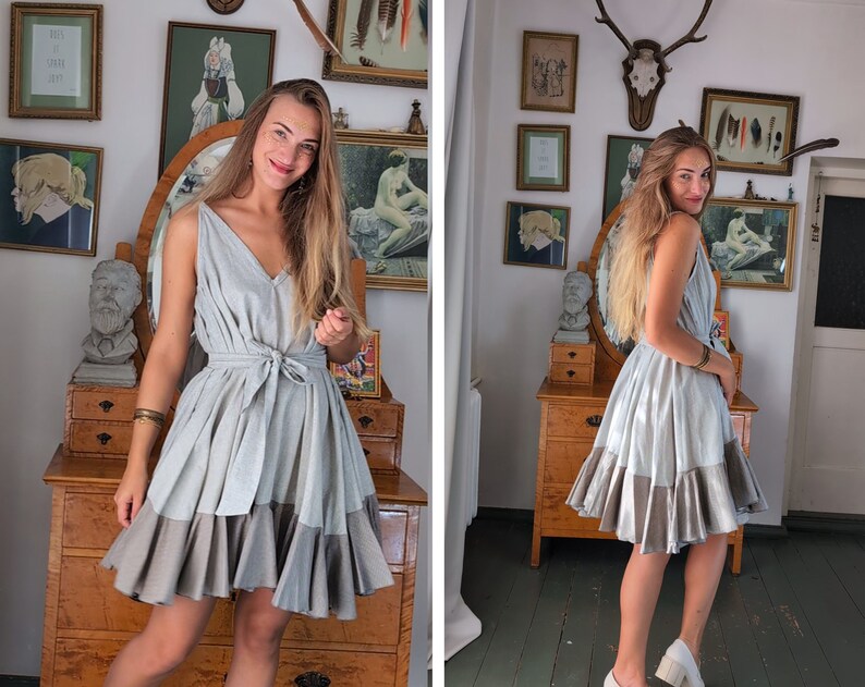 May include: A light gray sleeveless dress with a V-neck and a tie-waist. The skirt has a tiered design with a darker gray bottom. The dress is knee-length and appears to be made of a lightweight fabric. The model is wearing white shoes.