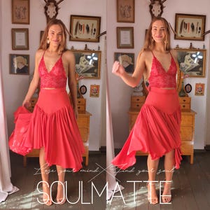 Puede incluir: Una mujer lleva un top rojo de encaje y una falda roja asimétrica. La falda tiene un diseño fluido y está hecha de una tela ligera. La mujer está de pie en una habitación con un suelo de madera y una variedad de objetos decorativos en las paredes. El texto "Love your mind. Find your soul. SOULMATE" es visible en el suelo frente a la mujer.
