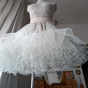 May include: A white tulle petticoat with multiple layers of ruffles. The petticoat has a white elastic waistband and is made of soft, sheer fabric.