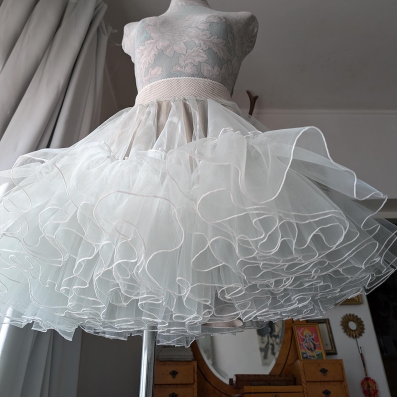 May include: A white tulle petticoat with multiple layers of ruffles. The petticoat has a white elastic waistband and is made of soft, sheer fabric.