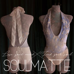 May include: A light blue and cream bodysuit featuring a deep halter neckline, intricate floral lace appliqu&eacute;s, and a tie-back closure. The garment displays the text "Lose your mind. Find your soul. SOULMATTE" across the front and back view.
