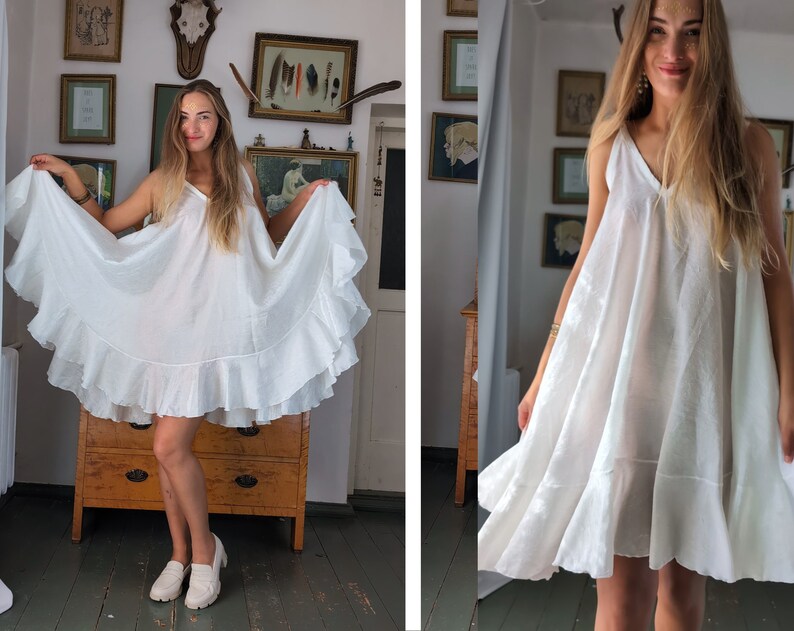 May include: A white, sleeveless dress with a V-neck and a tiered, ruffled hem. The dress is made of a lightweight fabric and falls to mid-thigh. The model is wearing white loafers.