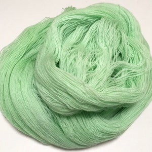 May include: A large skein of light green yarn, tightly wound and ready for crafting. The yarn has a soft, pastel color, perfect for knitting or crocheting projects. The texture appears smooth and delicate.