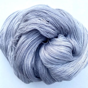 May include: A skein of soft, light gray yarn. The yarn is made of natural fibers and is perfect for knitting or crocheting.