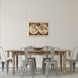 May include: A vintage world map print hangs above a rustic wooden dining table with four gray metal chairs. The map is framed in a simple wooden frame and features a detailed depiction of the world with landmasses and oceans.