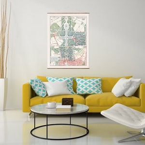 May include: A vintage map of Paris, France, from 1900, hanging on a white wall above a yellow sofa with white and blue patterned pillows. A white coffee table with a black metal frame sits in front of the sofa.