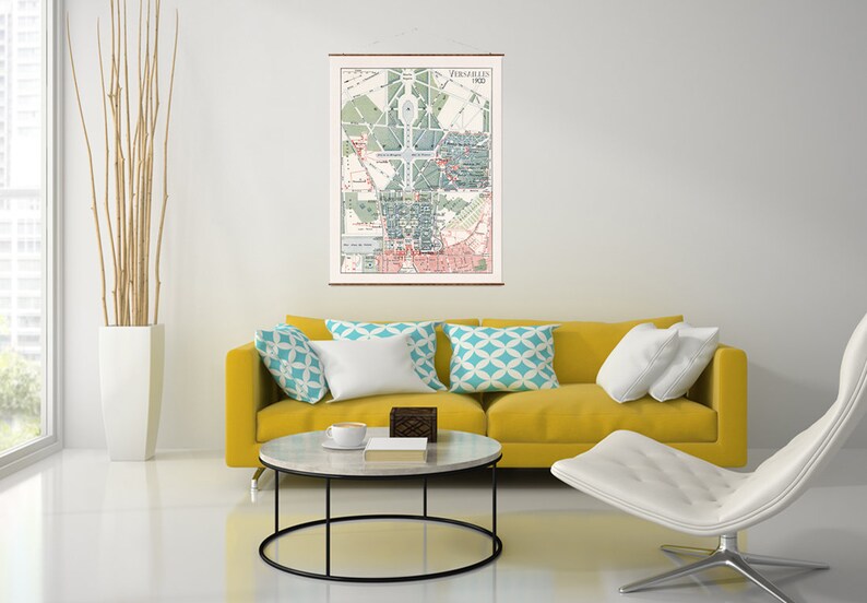 May include: A vintage map of Paris, France, from 1900, hanging on a white wall above a yellow sofa with white and blue patterned pillows. A white coffee table with a black metal frame sits in front of the sofa.