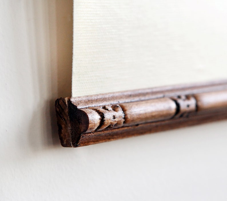 May include: Close-up of the bottom edge of a framed artwork. The frame is made of dark wood with an ornate design.