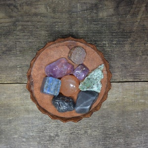 May include: A collection of seven colorful gemstones, including amethyst, lapis lazuli, and carnelian, arranged in a circular pattern on a brown leather coaster.