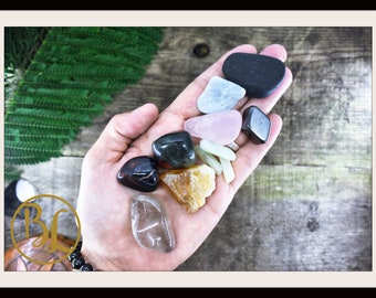 May include: A collection of tumbled stones in various colors and shapes, including clear quartz, rose quartz, black obsidian, and green aventurine.