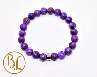 May include: A beaded bracelet featuring round, polished beads in shades of purple and brown. The bracelet is strung on a stretchy cord and includes a silver-colored metal accent. The beads have a marbled appearance. The bracelet is displayed on a white background.
