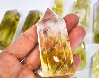 May include: A clear quartz crystal point with yellow and brown inclusions. The crystal is pointed at the top and has a flat base. It is being held in a hand.