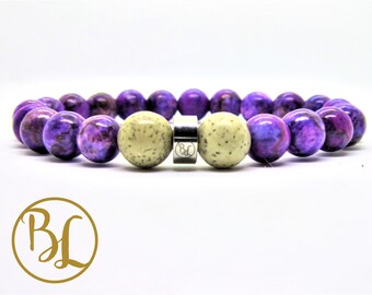 May include: A beaded bracelet featuring large, round beads in shades of purple and cream. The purple beads have a marbled appearance, while the cream beads are speckled. A silver-toned clasp secures the bracelet. The bracelet is displayed on a white background.