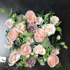 May include: A pink and white floral arrangement with roses, greenery, and small flowers. The arrangement is in a square shape and is perfect for a wedding or other special occasion.