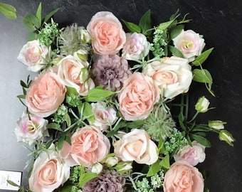 May include: A pink and white floral arrangement with roses, greenery, and small flowers. The arrangement is in a square shape and is perfect for a wedding or other special occasion.