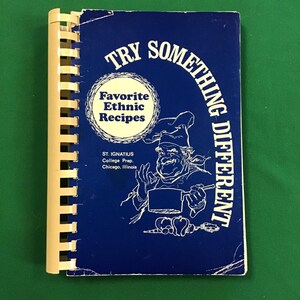 May include: A blue spiral-bound cookbook titled TRY SOMETHING DIFFERENT Favorite Ethnic Recipes. The cover features a white line-art illustration of a chef holding a pot, with text identifying St. Ignatius College Prep, Chicago, Illinois.