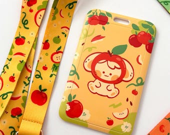 May include: Yellow lanyard and cardholder with an apple design. The cardholder features a cartoon character with an apple hat. The lanyard and cardholder are decorated with red apples, apple slices, and green leaves.