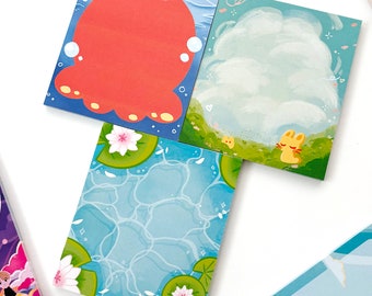 May include: A set of four square sticky notes with different illustrations. One note features a red cartoon octopus, another has a white cloud with a yellow rabbit, a third has a blue water pattern with lily pads, and the last one has a blue sky with a white cloud.