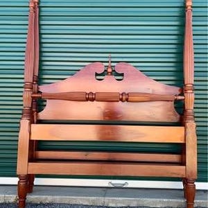 May include: A wooden four-poster bed frame with a reddish-brown finish. The headboard features a decorative cutout design and horizontal slats. The bed frame has four tall posts and is made of solid wood.