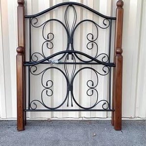May include: A black wrought iron headboard with decorative scrollwork and two wooden posts. The headboard is a dark color and has a classic design. The wooden posts are a medium brown color.