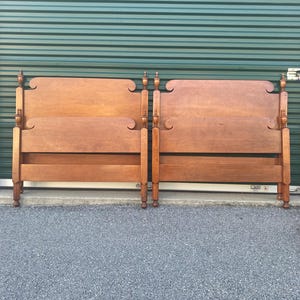 May include: A pair of matching twin-sized wooden bed headboards and footboards featuring a warm brown finish. Each piece displays a curved top rail, smooth horizontal panels, and vertical posts topped with decorative finial accents.