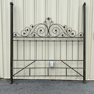 May include: A dark bronze-colored metal headboard featuring two tall vertical posts on each side. The upper section displays intricate scrollwork and curved metal detailing, while the lower portion consists of straight vertical bars and horizontal rails.