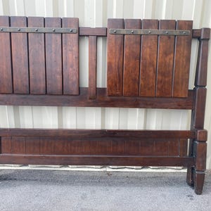 May include: A dark brown wooden headboard with a rectangular design. The headboard features two rectangular panels with vertical wooden slats and decorative metal accents. The frame is made of solid wood with a sturdy construction.
