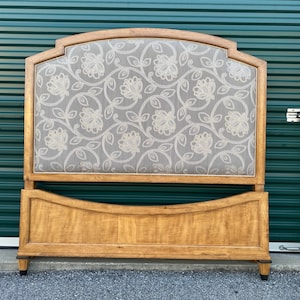 May include: A wooden headboard and footboard set featuring a light brown finish with a visible wood grain. The headboard has an arched top and a central upholstered panel in a grey fabric with a white embroidered floral vine pattern.