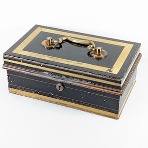May include: Black antique cash box with gold trim and handle. The rectangular box has a keyhole and a hinged lid. The gold trim outlines the top and sides of the box, and the handle is also gold.