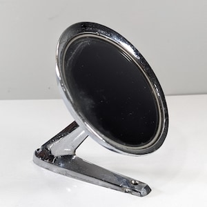 May include: Chrome side mirror with a black reflective surface. The mirror has a rounded oval shape and is mounted on a chrome arm. The mirror is designed for a vehicle.