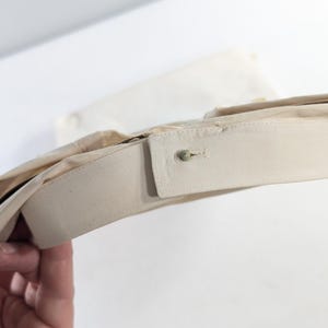 May include: Close-up of a beige dress shirt collar with a buttoned closure. The collar is folded over, revealing the inside lining. The shirt appears to be made of a light, possibly cotton, fabric.