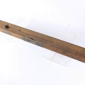 Puede incluir: Un nivel de madera vintage con detalles en latón. El nivel tiene un solo vial de burbuja y mide aproximadamente 61 cm de largo.