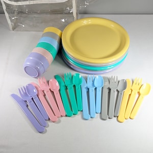 May include: A set of pastel-colored plastic plates, bowls, forks, spoons, and knives. The plates are stacked in a tower, and the utensils are arranged in a row.