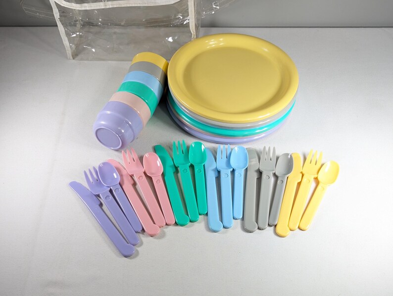 May include: A set of pastel-colored plastic plates, bowls, forks, spoons, and knives. The plates are stacked in a tower, and the utensils are arranged in a row.