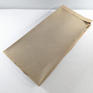 May include: A rectangular, open cardboard box with a light brown exterior. The box is slightly damaged on one side, revealing the corrugated interior. The box is empty and sits on a white surface.