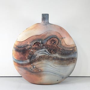 May include: A large, handcrafted ceramic vase with a rounded body and a narrow neck. The vase features a textured surface with layered bands of color, including shades of peach, brown, and gray. The design incorporates spiral and linear patterns, creating a unique, artistic aesthetic.