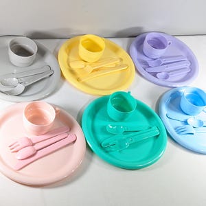 May include: A set of six colorful plastic plates and cups with matching spoons and forks. Each set includes a plate, cup, spoon, and fork in a different color: gray, yellow, purple, blue, pink, and green.
