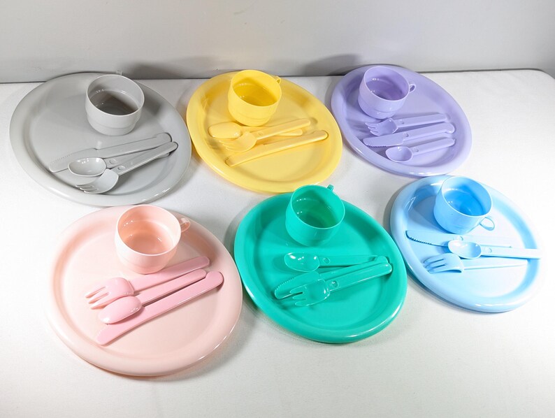 May include: A set of six colorful plastic plates and cups with matching spoons and forks. Each set includes a plate, cup, spoon, and fork in a different color: gray, yellow, purple, blue, pink, and green.