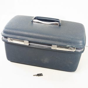 May include: A rectangular navy blue hard-shell train case with a textured finish, featuring a dark blue handle with chrome accents, two silver-toned metal latches with integrated keyholes, and a single small metal key positioned in front of the case.