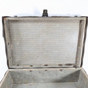 May include: An open rectangular trunk with a dark brown exterior and a light gray fabric-lined interior. The trunk features a wooden frame structure, a metal latch mechanism at the top center, and visible metal rivets along the inner edges.
