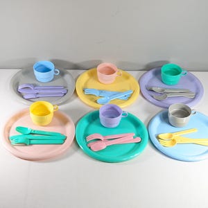 May include: A set of pastel-colored plastic children's dishes, including plates, cups, forks, and spoons. The set includes six plates, six cups, six forks, and six spoons.
