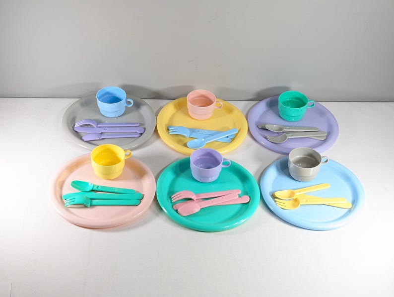 May include: A set of pastel-colored plastic children's dishes, including plates, cups, forks, and spoons. The set includes six plates, six cups, six forks, and six spoons.