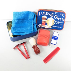 May include: A shaving kit featuring a blue metal tin with the text James & Owen of Suffolk High St Barber, a blue towel, two red disposable razors, a shaving brush with a brown handle, a red soap container, and a box labeled Shave Stick.