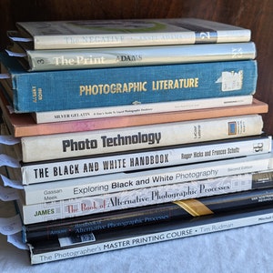 Op de afbeelding: Een stapel van tien fotografieboeken met titels zoals "The Negative", "The Print", "Photographic Literature", "Photo Technology", "The Black and White Handbook", "Exploring Black and White Photography", "The Book of Alternative Photographic Processes", "Handbook of Alternative Photographic Processes" en "The Photographer's Master Printing Course".