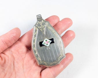 May include: A silver locket pendant with an ornate design and a black and white enamel rose with pink accents.