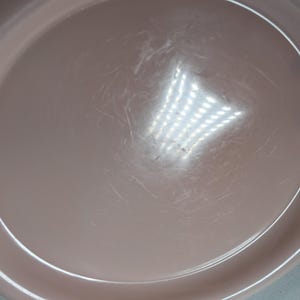 May include: A plain, light pink, round, plastic serving plate with a slightly raised rim.